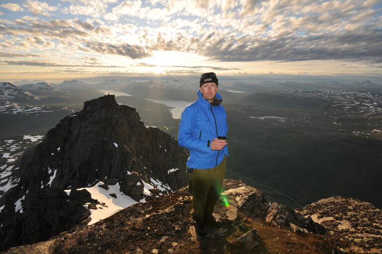 Mann på toppen av ett fjell med utsikt over fjorden