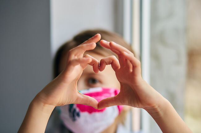 Bilde av jente med munnbind som lager hjerteform med hendene.