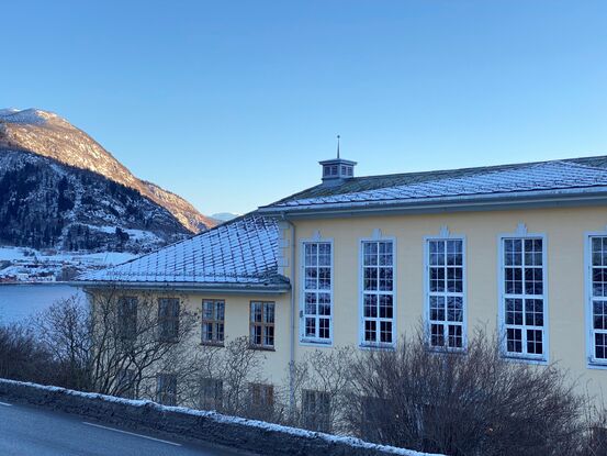 Tinghuset på Leikanger sett mot Hermansverk med sol på snødekte toppar.