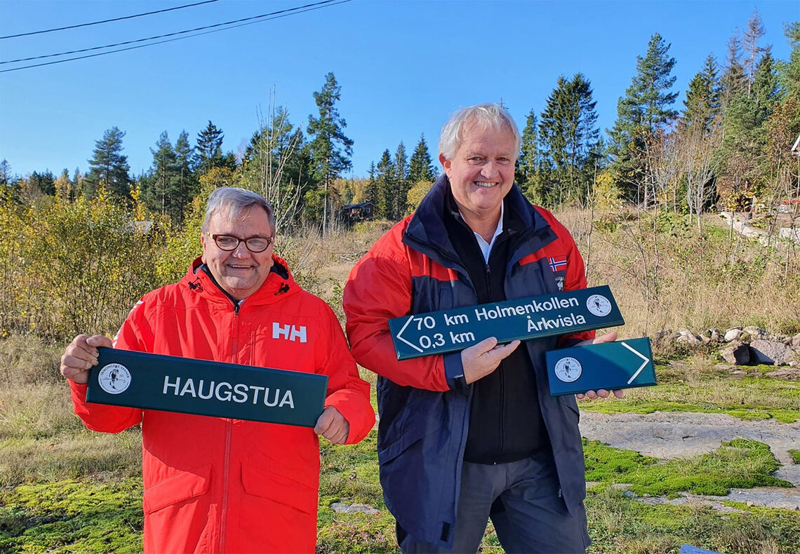Ildsjelene Knut Olaf Kals (til venstre) og Marius Morin viser fram noen av skiltene som skal guide både fotturister og ultraløpere fra Lier til Holmenkollen. (Foto: Gjermund Sørstad)
