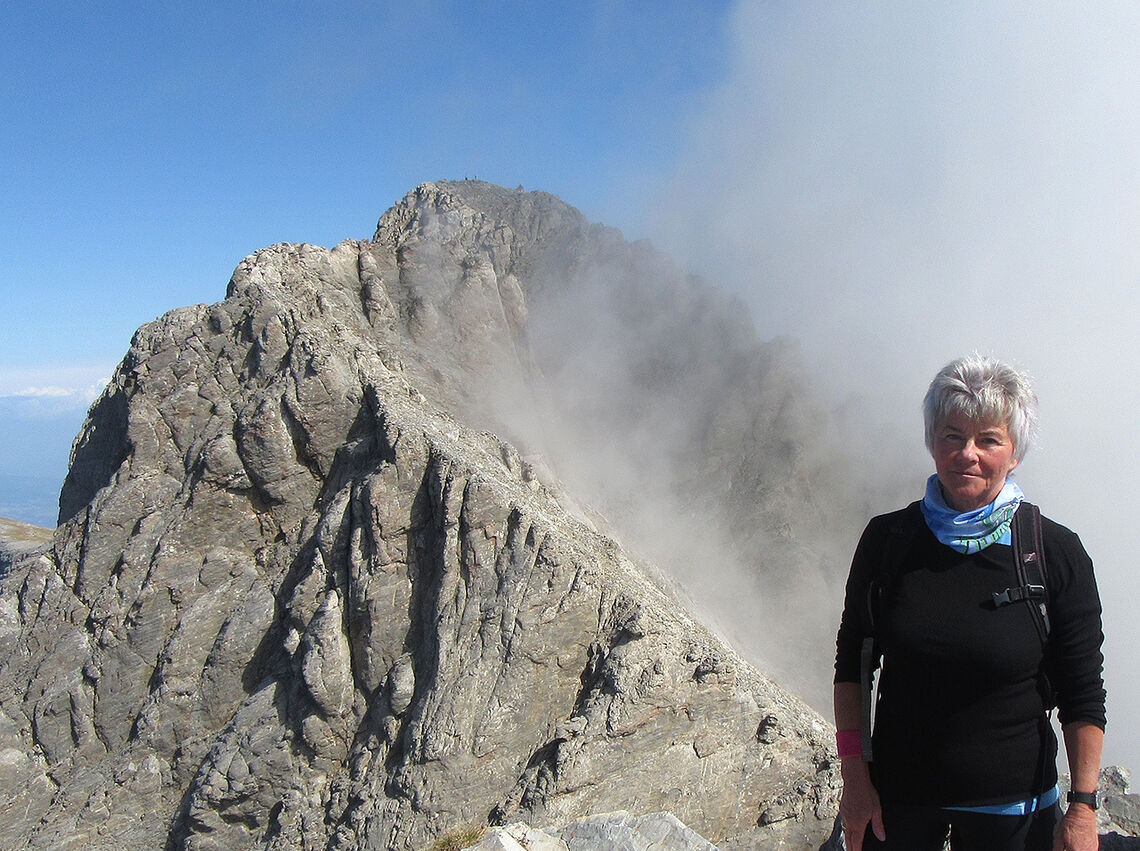 Høyt oppe: Artikkelforfatter Else Husa står på toppen av Skala (2885moh.) med den høyeste toppen Mytikas (2917 moh.) i bakgrunnen. Avgrunnen mellom de to toppene kommer ikke frem på bildet. (Foto: privat)
