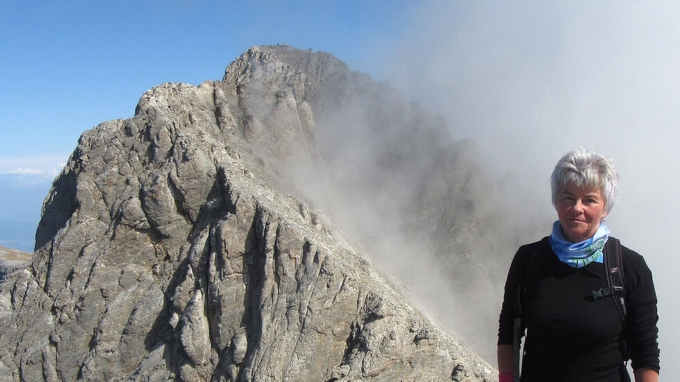 Høyt oppe: Artikkelforfatter Else Husa står på toppen av Skala (2885moh.) med den høyeste toppen Mytikas (2917 moh.) i bakgrunnen. Avgrunnen mellom de to toppene kommer ikke frem på bildet. (Foto: privat)