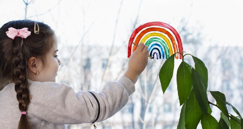 Illustrasjonsbilde av karantenetilværelse - en jente som tegner regnbue på et vindu