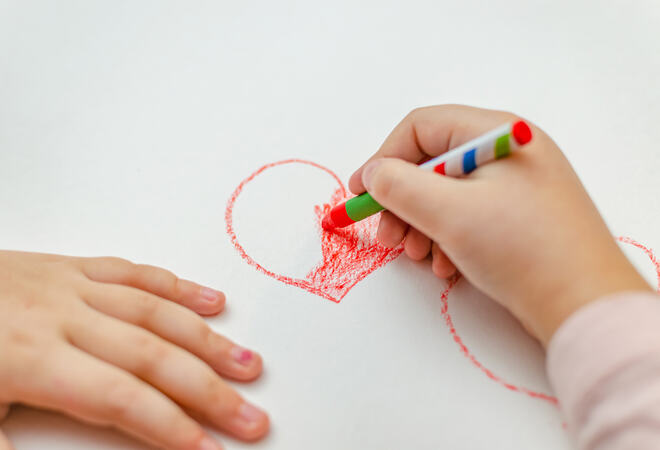 A little girl is drawing a heart with red chalk - high angle image with selective focus. Valentine