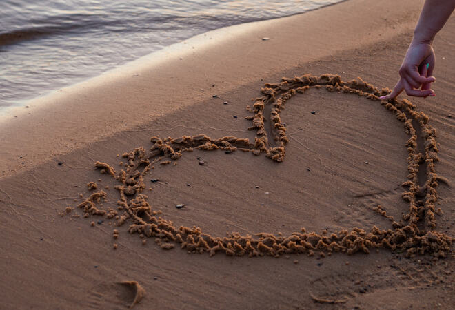 Close up view of woman hand drawing heart with finger on the san