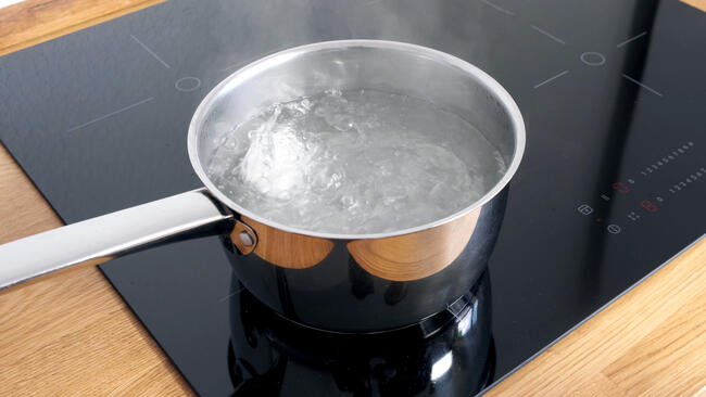 Chicken eggs boiling in stainless steel pan in water.