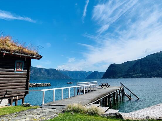 Utsikt frå hotellhagen mot brygge, fjord og fjell.