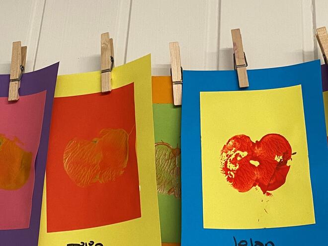Barnehagekunst. Fargerike ark med trykk av eple som heng på ei snor.