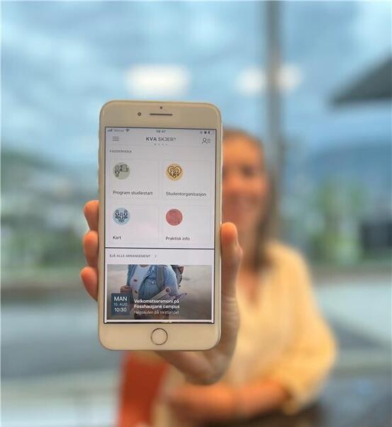 Bilete av ein person som held fram ein mobil med appen "Kva skjer" på skjermen.