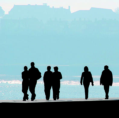 Silhuetter av 6 personer som går ut mot havet på en solrik dag