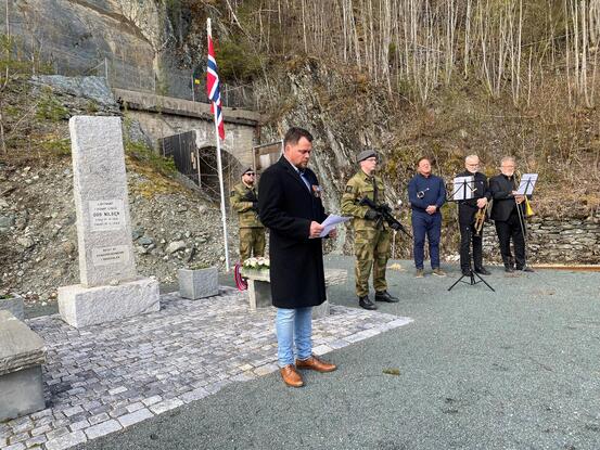 Leder av veteranforeninga i Orkland og omegn Trond Melting holdt tale under markeringen i 2022. Foto: Arnt Tronvoll/Orkland kommune Mann i sort jakke holder tale, mens militærkledde menn holder vakt. Tre mannlige musikere i bakgrunnen.