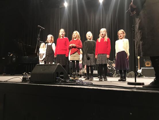 Seks jenter i barneskulealder kledde i svart, kvitt og raudt står framme på scenekanten og syng.