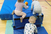 Tre barn som klatrer på madrasser i gymsal