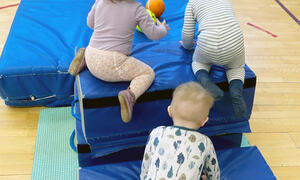 Tre barn som klatrer på madrasser i gymsal
