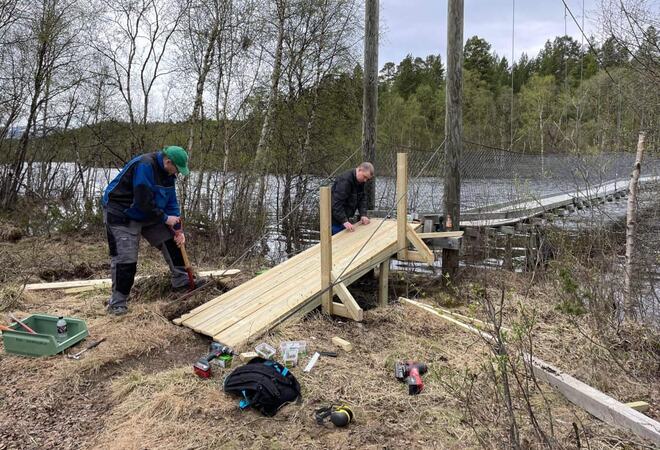 Bilde av to menn som jobber med en rampe laget av tre som leder opp til en hengebro