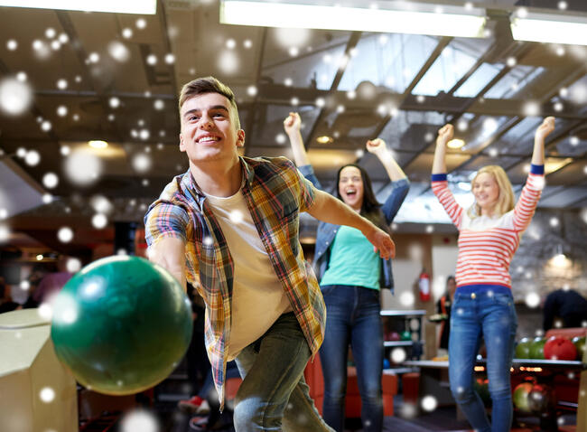Gutt kaster en bowlingkule, mens to smilende jenter står i bakgrunnen