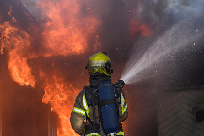 Brannkonstabel som spruter vann på et brennende hus