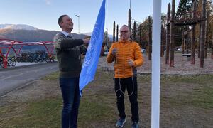 To menn heiser det blå FN-flagget utanfor Leikanger barneskule.