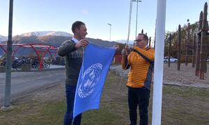 To menn står klare med det blå FN-flagget utanfor Leikanger barneskule.