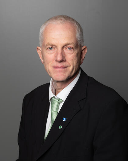 Mann med dress, grønt slips og grått hår.