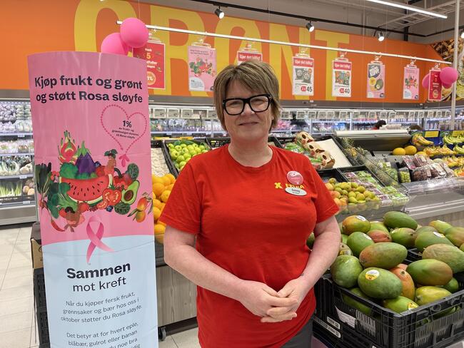 Kvinne i rød T-skjorte foran en fruktdisk i butikk