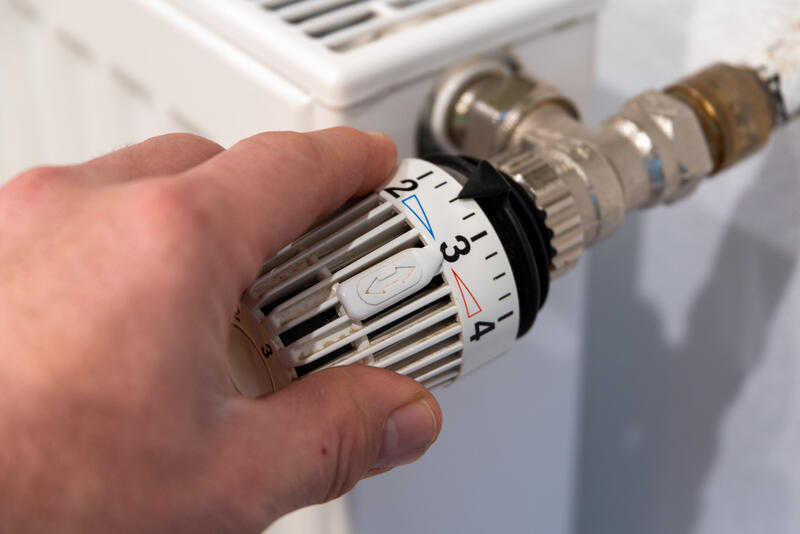 En hånd skrur opp termostat på en radiator