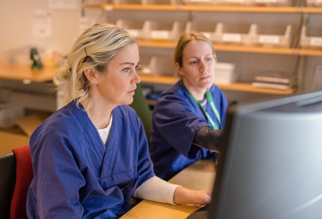 To sykepleiere sitter foran en PC