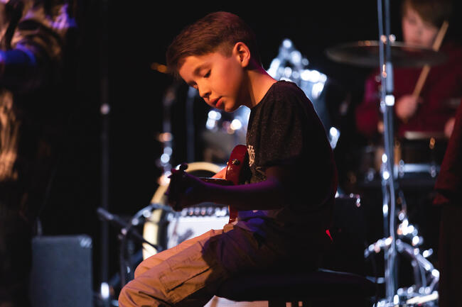 Ung gutt som spiller gitar i et mørkt lokale