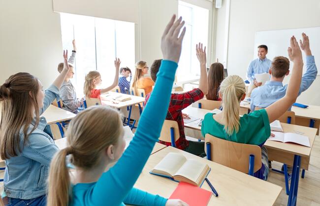 Skoleelever som rekker opp hånda i et klasserom. Illustrasjonsfoto: Mostphotos.