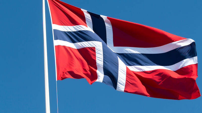 Det norske flagget vaier i vinden med blå himmel i bakgrunn