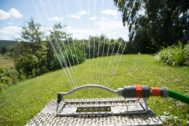 En hagespreder som sprayer vann. Den er festet til en hageslange og plassert på en plen. Vannstrålene sprer seg jevnt utover et grønt område.