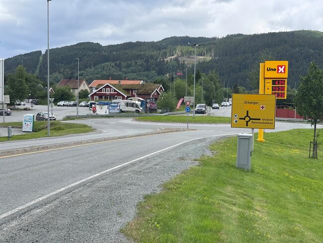 Bildet viser en rundkjøring. Det er et gult skilt for Uno X bensinstasjon med prisene for bensin og diesel. Bakgrunnen viser skogkledde åser. Det er også veiskilt som peker mot Orkanger, Ulvåsen og Rømmesbakkan.