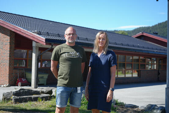 Erlend Ysland, rektor ved Lensvik og Lysheim skoler, her sammen med rektor ved Evjen skole, Drude Tøndel. De står utenfor et stort bygg og ser inn i kamera.