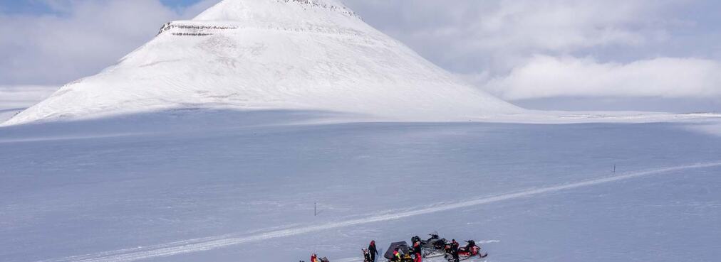 bilde av snødekt område med fjell i bakgrunnen og snøskutere på tur