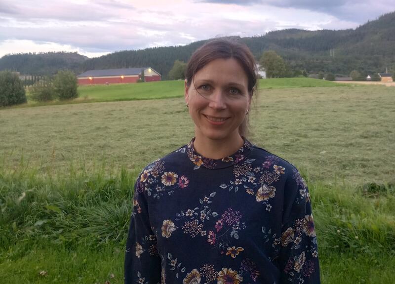 Anne Lise Dahl står foran en kornåker med et fjøs i bakgrunnen