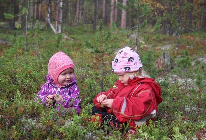 To barn sitter på bakken blant bærbusker