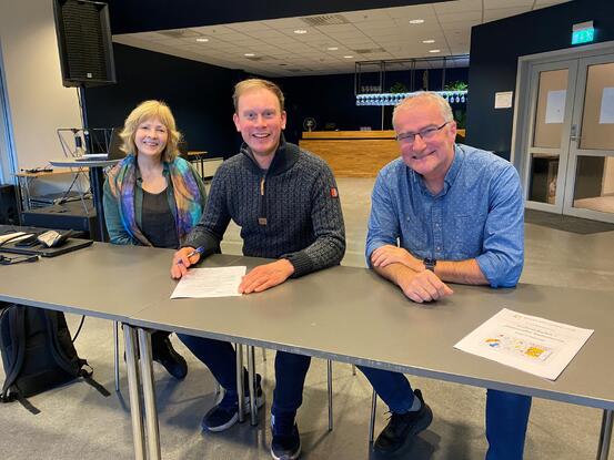 Tre personar sit ved eit bord og signerer eit dokument.