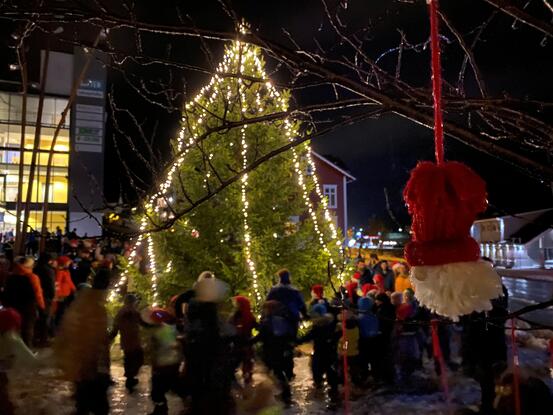 Tend julegran, folk som går rundt treet og ein heimelaga nisse som heng i eit tre.