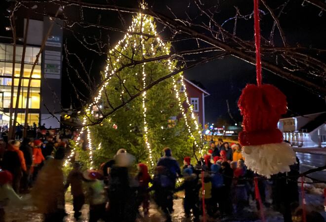 Tend julegran, folk som går rundt treet og ein heimelaga nisse som heng i eit tre.