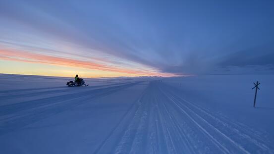 På bilde: Enslig skuter, med fører,  på vei over fjellet i solnedgang.. Foto : GN