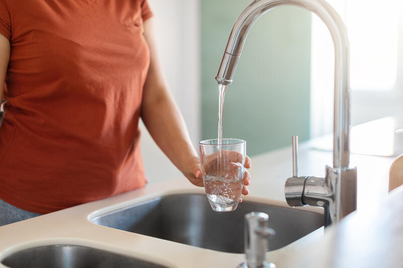Dame fyller vann i glass fra vannkranen