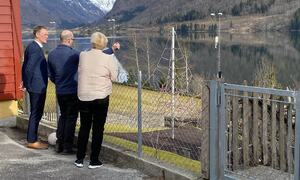 Tre personar ser på utsikt over fjord og fjell.