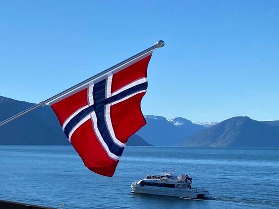 Balkongflagg, musikkbåt på fjorden, fjell og blå himmel
