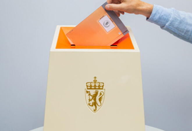 Ei hand som held i ein raud røystesetel som er halvveges nedi ei valurne