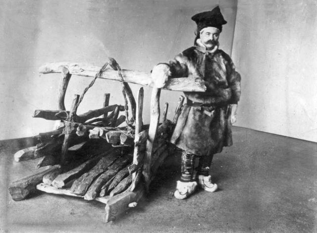 Svart/hviitt foto av Isak Saba i pesk ved dyrefelle av tre.