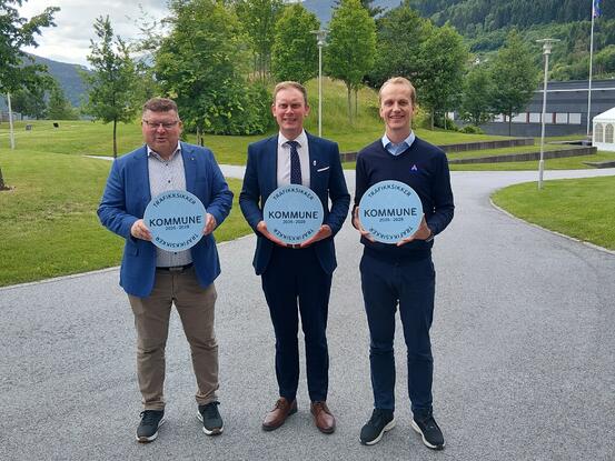 Tre menn står og held skilt med Trafikksikker kommune.