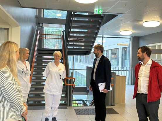 To kvinner i kvite sjukepleiaruniformar snakkar med to dresskledde menn