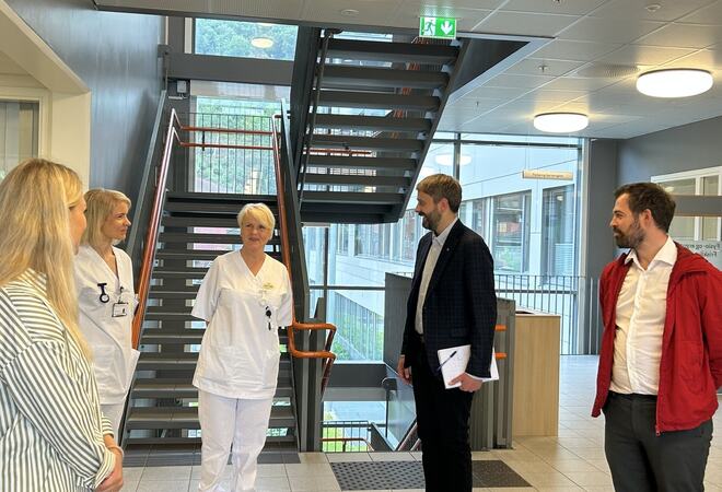 To kvinner i kvite sjukepleiaruniformar snakkar med to dresskledde menn