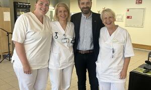 Mann i dress, helseminister Vestre, poserer smilande saman med tre kvinner i kvite uniformar