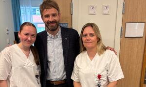 Dresskledd mann flankert av to kvinner i kvite uniformar